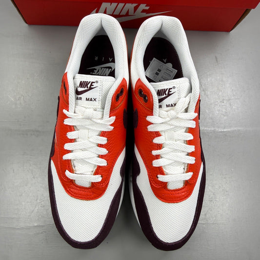 Nike Air Max 1 white trainers with burgundy accents and logo detail.