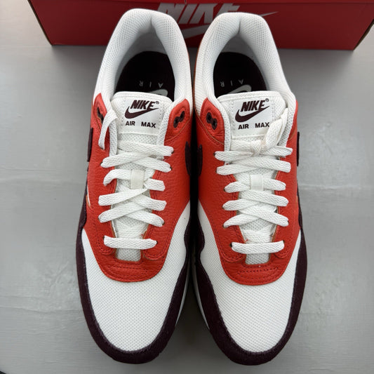 Nike Air Max 1 white trainers with burgundy and red accents, featuring logo details.