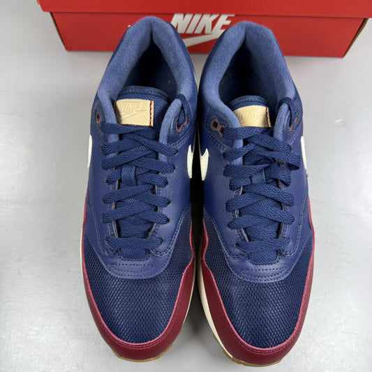 Nike Air Max 1 red trainers with navy accents and gum sole, featuring logo details.