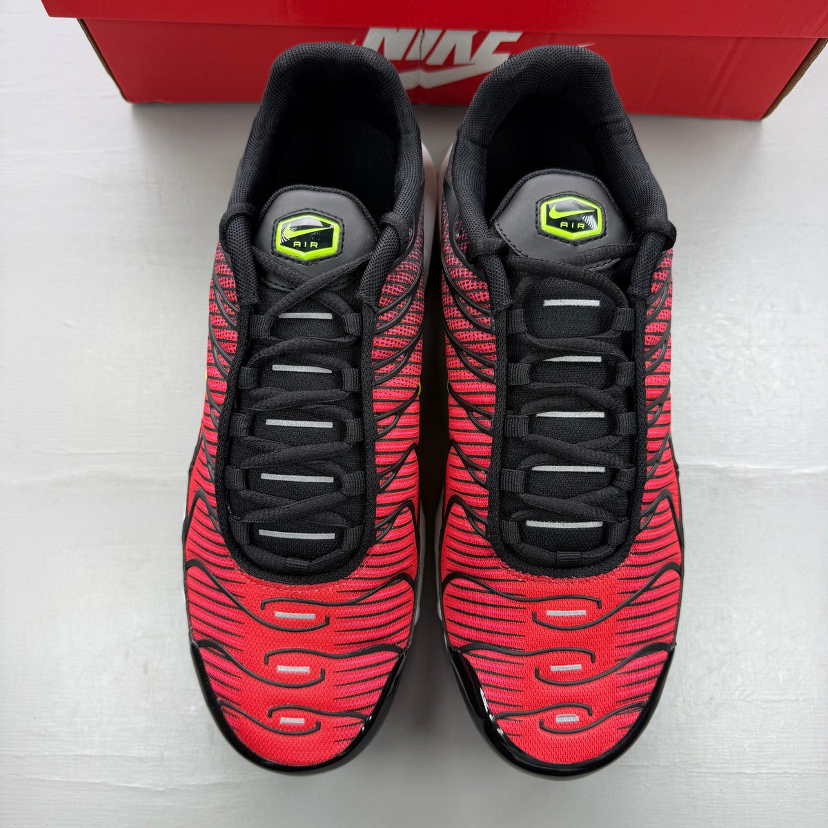 Nike Air Max Plus TN black trainers with light crimson and volt accents, logo on tongue.