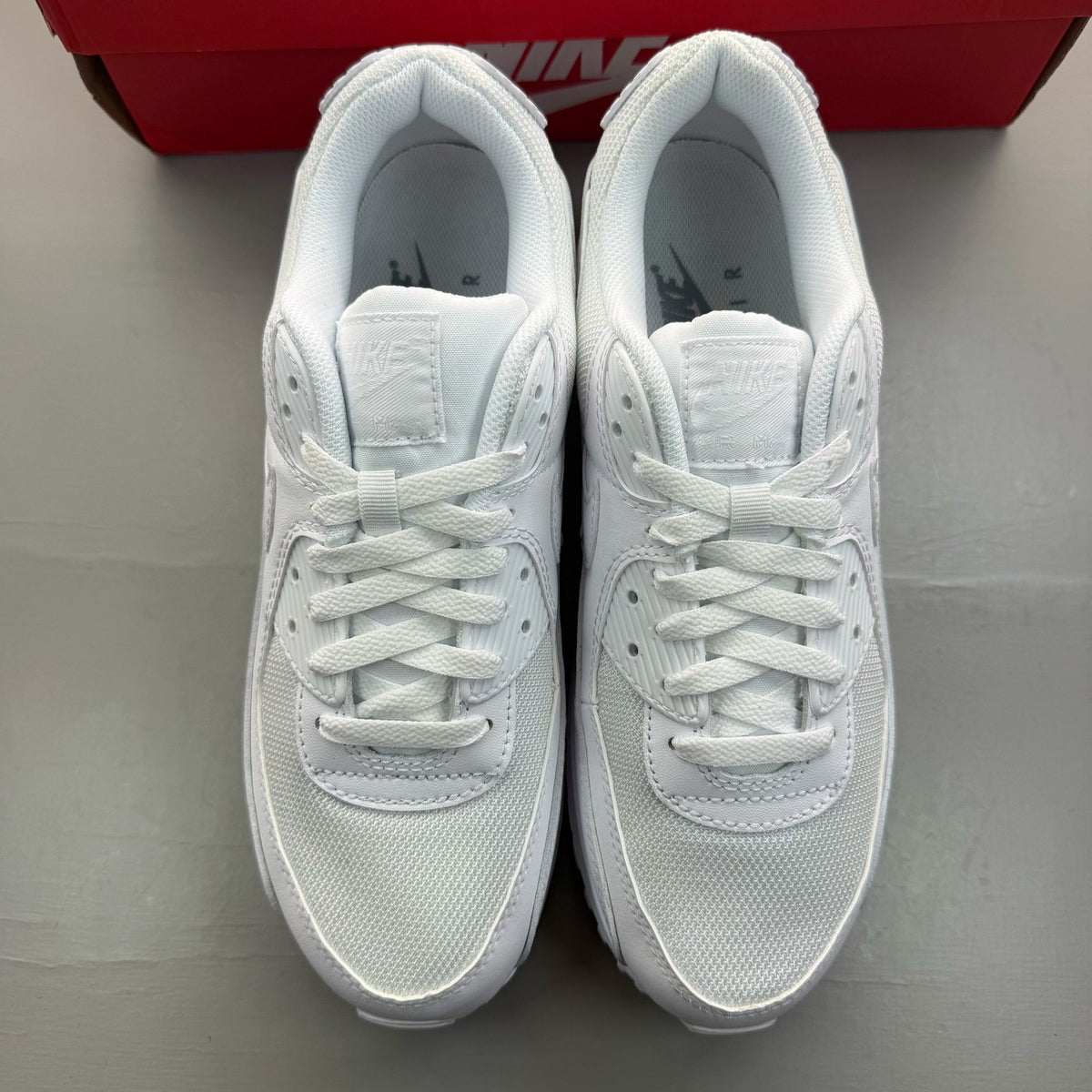 Nike Air Max 90 white trainers with iconic swoosh logo and breathable mesh material.