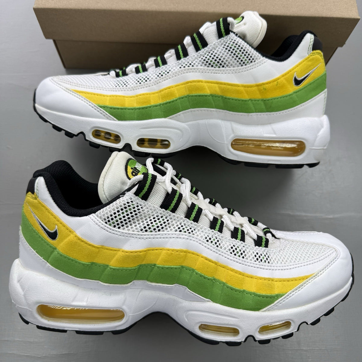 Nike Air Max 95 white trainers with green and yellow accents, featuring iconic logo details.