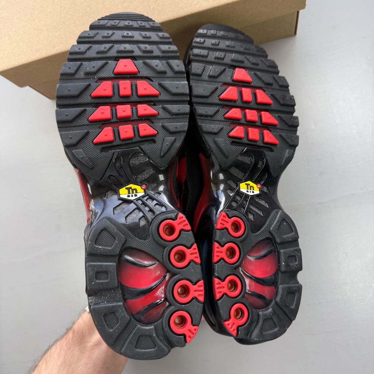 Nike black Air Max Plus TN trainers with reflective accents and red detailing.