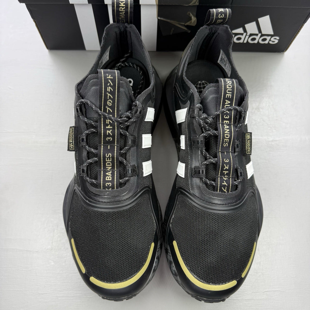 Adidas black trainers with white and gold accents, featuring a sleek design and logo.
