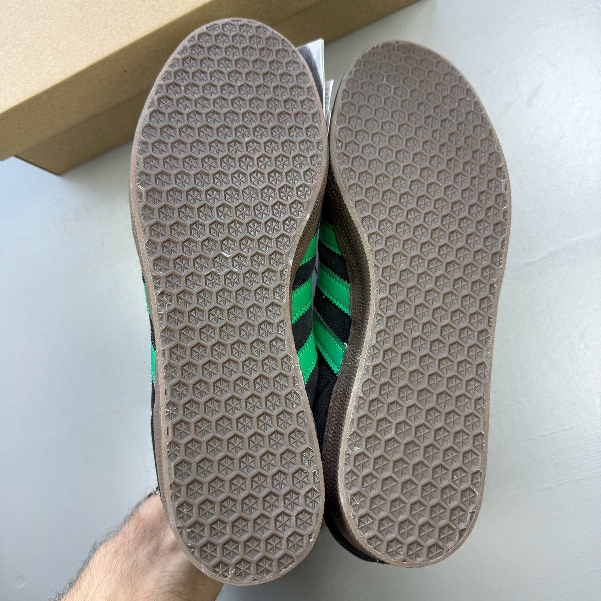 Adidas black Gazelle trainers with green accents and classic logo detailing.
