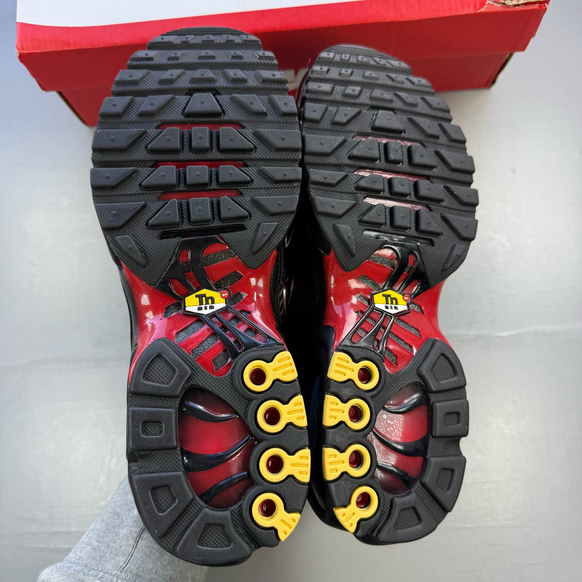 Nike Air Max Plus TN black trainers with university red accents and visible logo details.