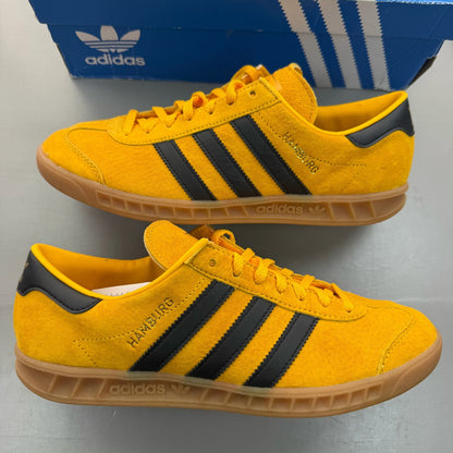 Adidas yellow trainers with black and gold accents, featuring iconic logo detail.