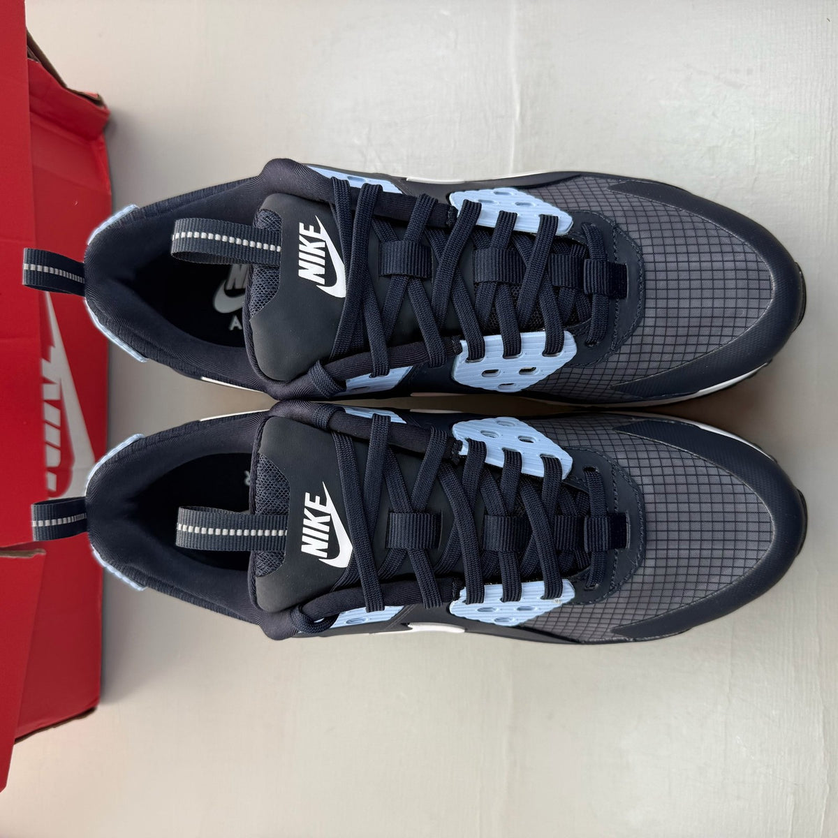 Nike Air Max 90 blue trainers with white accents and logo detail.