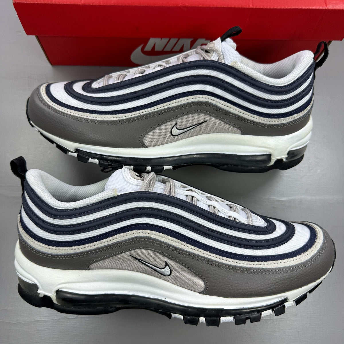 Nike Air Max 97 white trainers with grey and navy accents, featuring iconic swoosh logo.