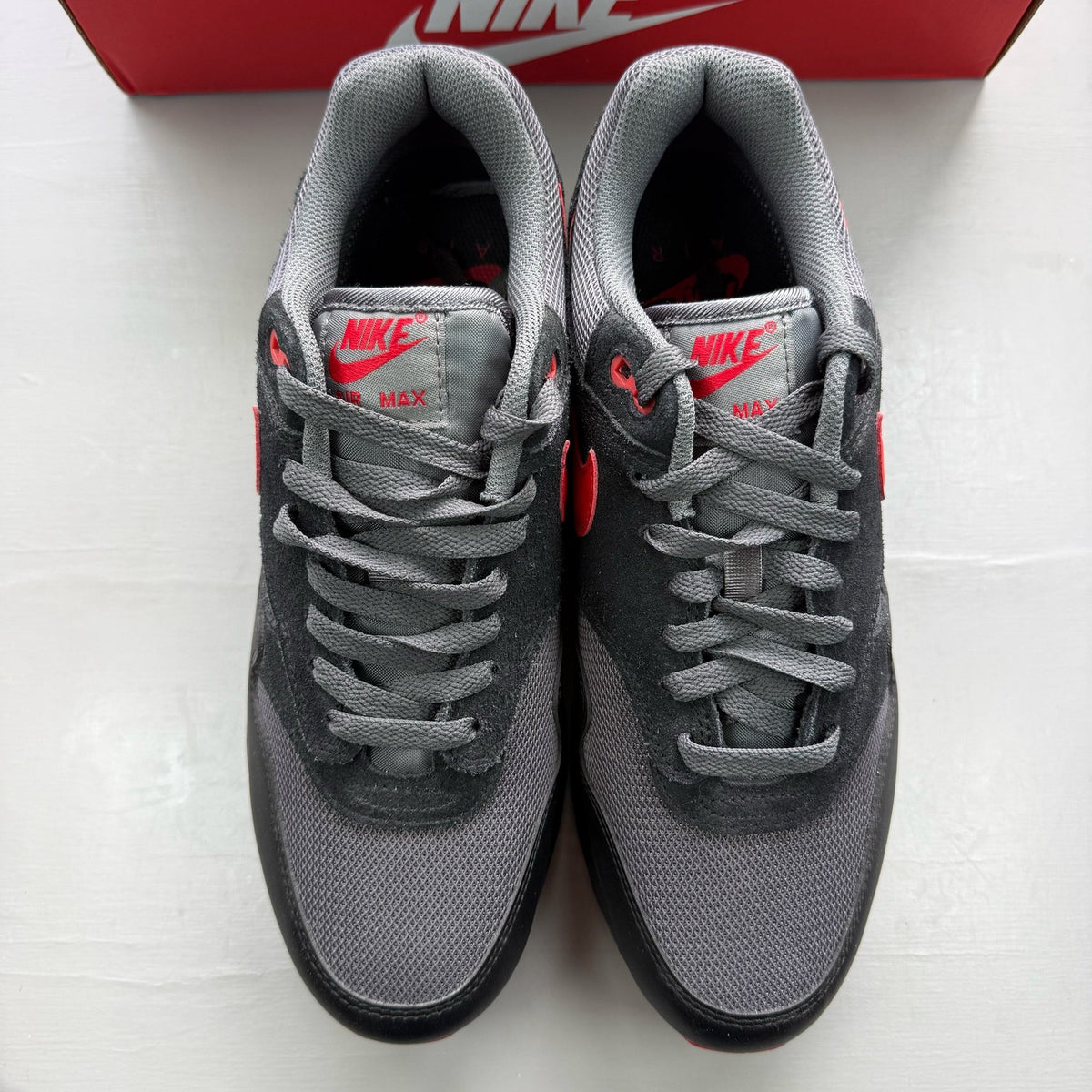 Nike black Air Max 1 trainers with red accents and logo detail.