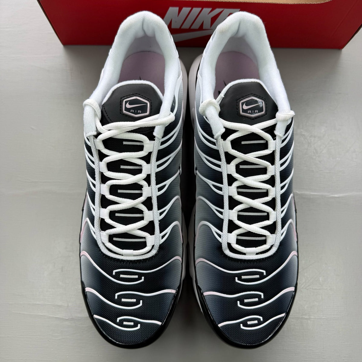 Nike Air Max Plus TN black trainers with pink accents and signature swoosh logo.