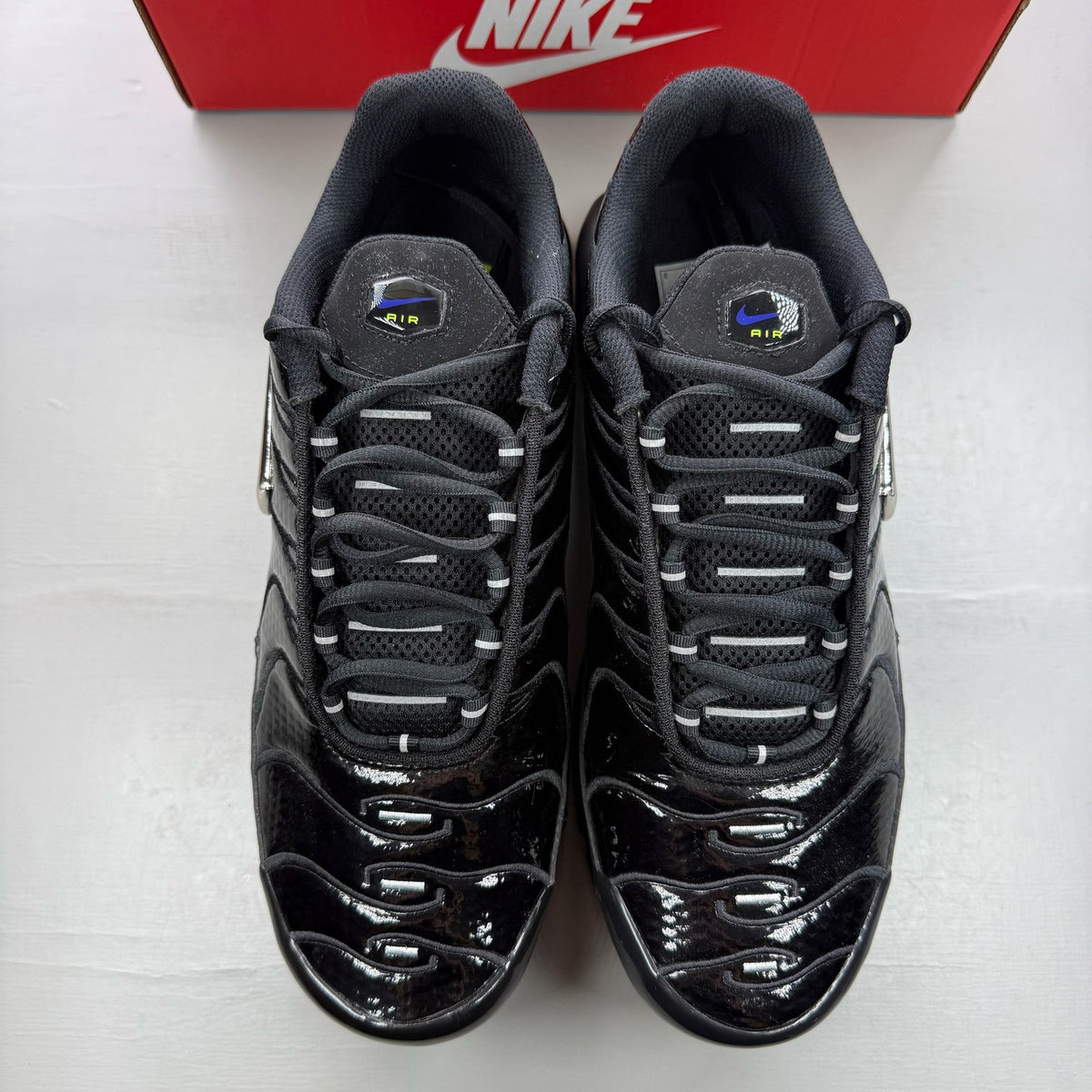 Nike black Air Max Plus TN trainers with chrome accents and vibrant volt detailing.