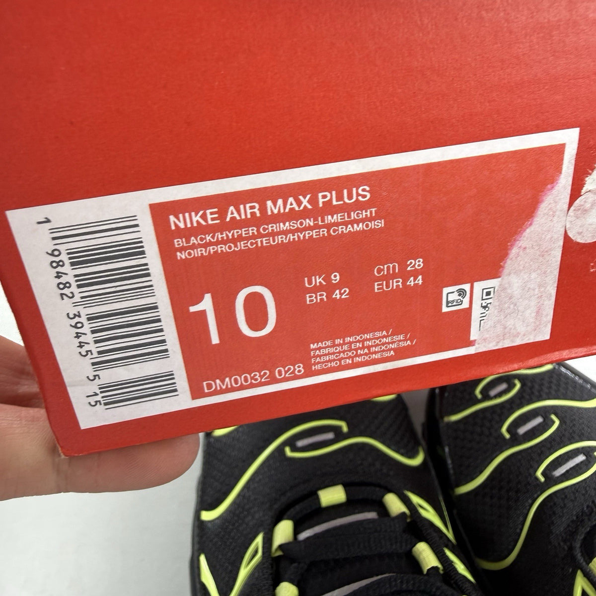 Nike Air Max Plus TN black trainers with vibrant orange and volt accents, mesh material.