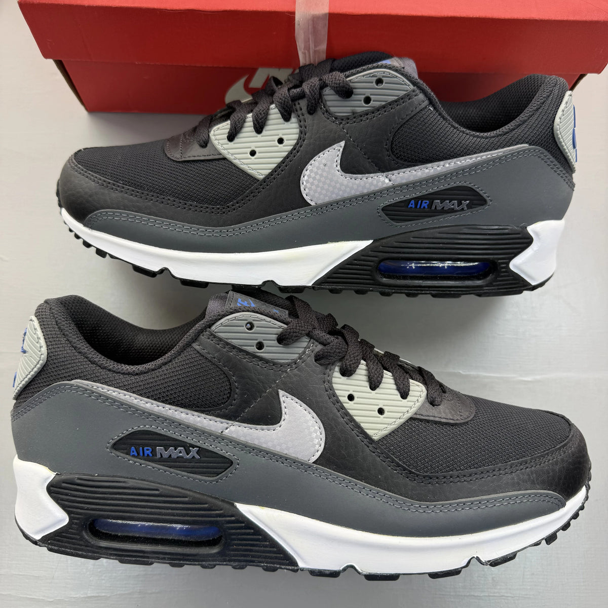 Nike Air Max 90 black trainers with grey and blue accents, featuring iconic logo details.