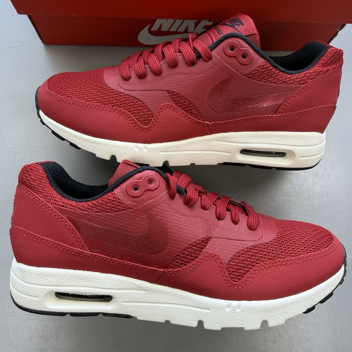 Nike Air Max 1 Ultra Essential red trainers with white and black accents, logo detail.
