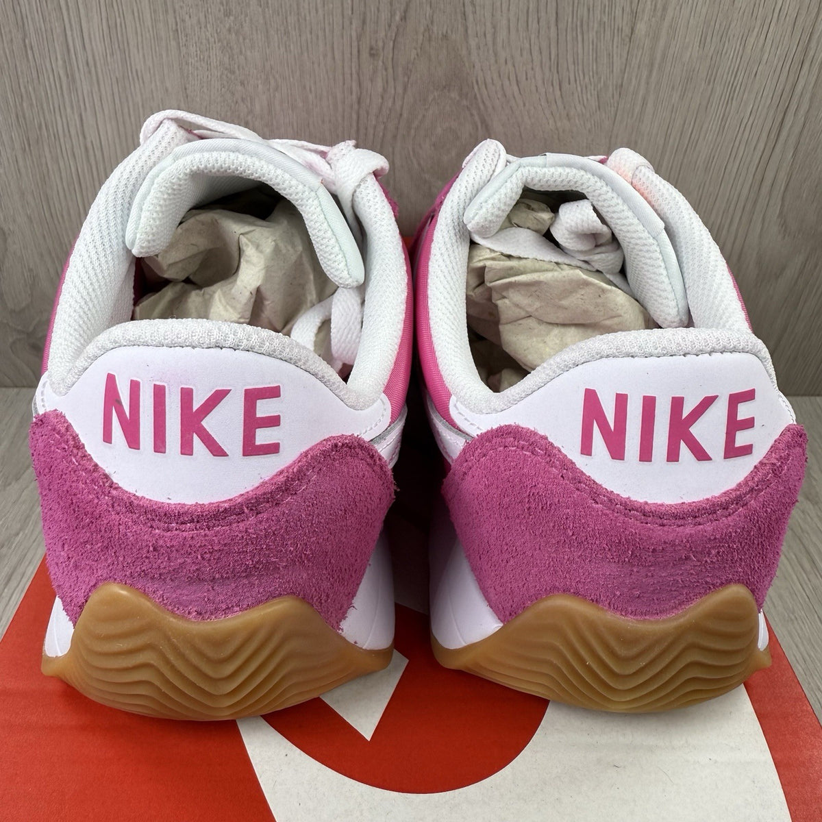Nike white trainers with pink accents and gum sole, featuring iconic swoosh logo.