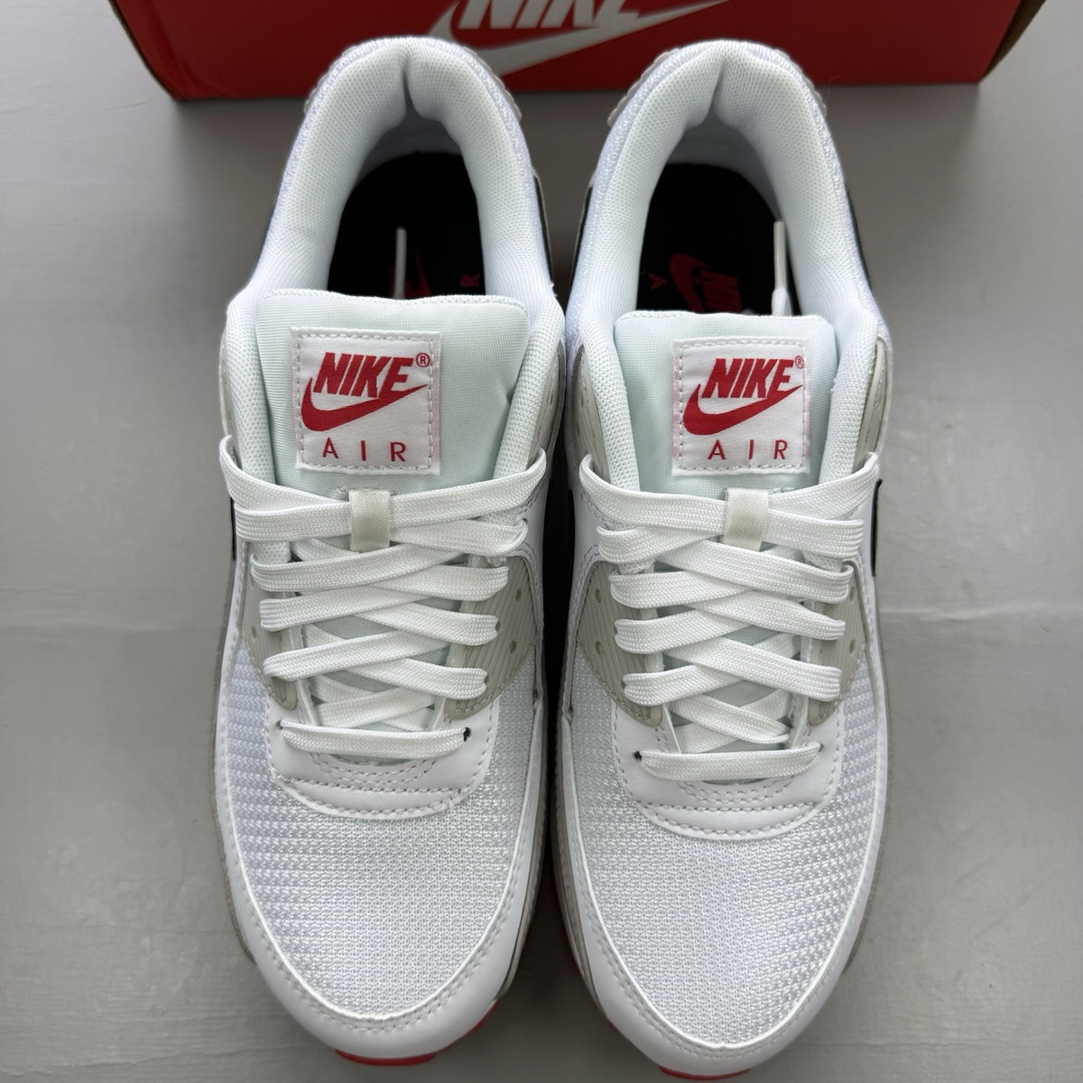 Nike Air Max 90 white trainers with black and red accents, featuring iconic logo and design.