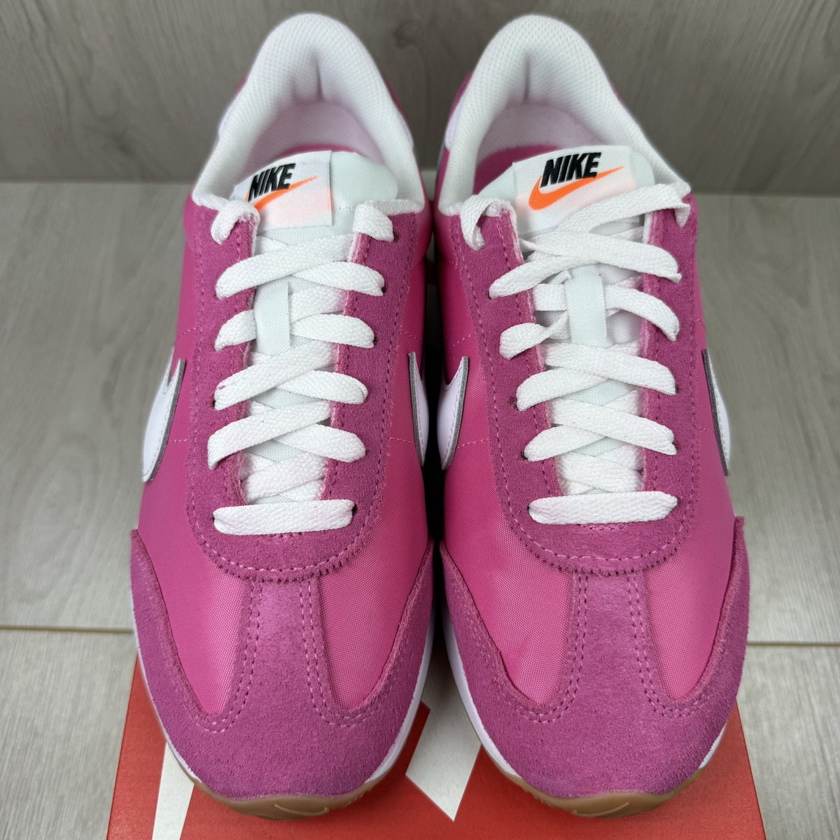 Nike white trainers with pink accents and gum sole, featuring iconic swoosh logo.
