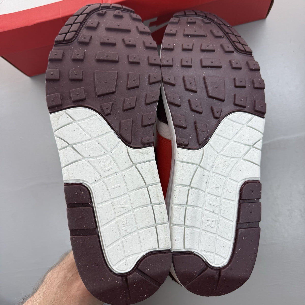 Nike Air Max 1 white trainers with burgundy and red accents, featuring logo details.