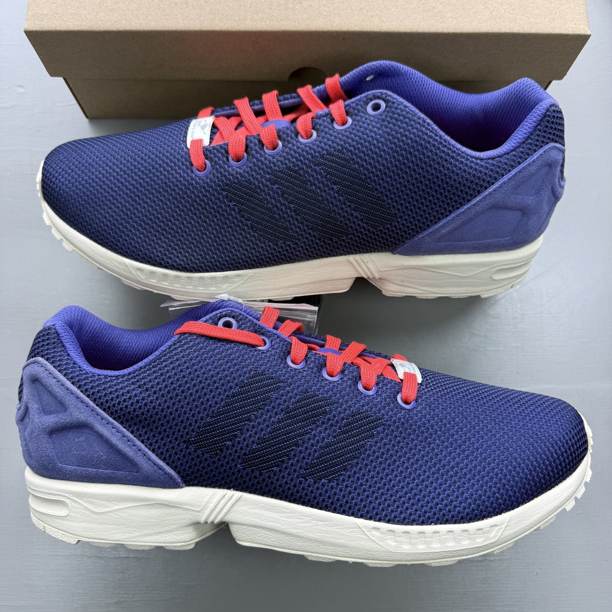 Adidas blue ZX Flux trainers with red and white woven pattern, logo on tongue.