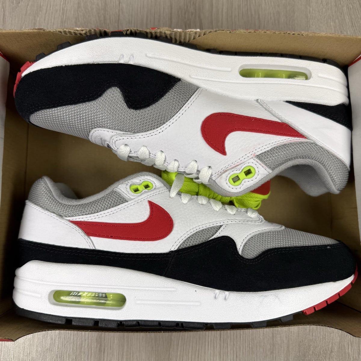 Nike Air Max 1 trainers white with chili volt accents and black detailing.