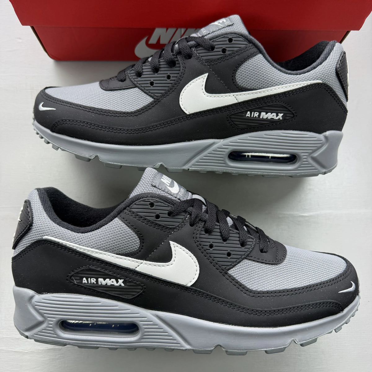 Nike Air Max 90 black trainers with smoke grey accents and logo detail.