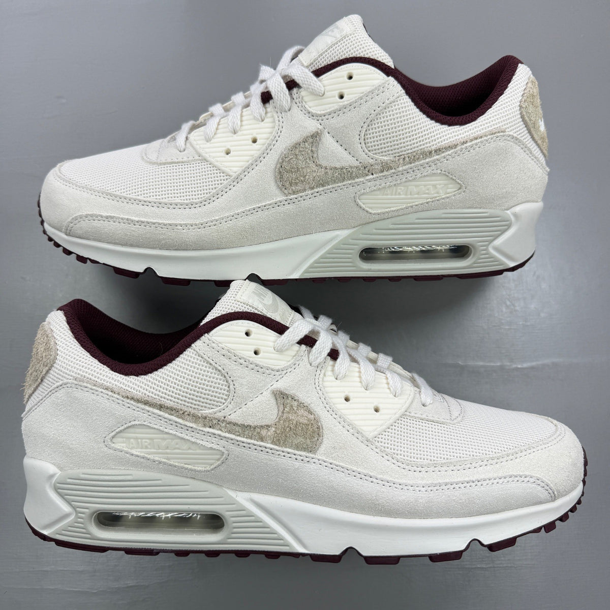Nike Air Max 90 white trainers with burgundy accents and signature swoosh logo.