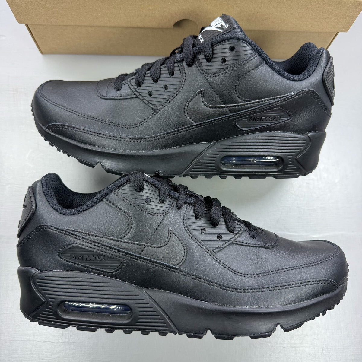 Nike Air Max 90 black leather trainers with iconic swoosh logo and textured design.