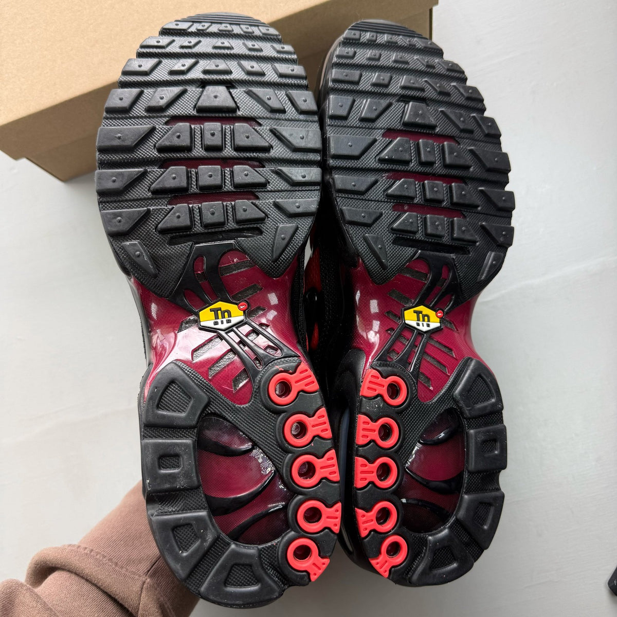 Nike Air Max Plus TN black trainers with crimson and noble red accents, mesh upper.