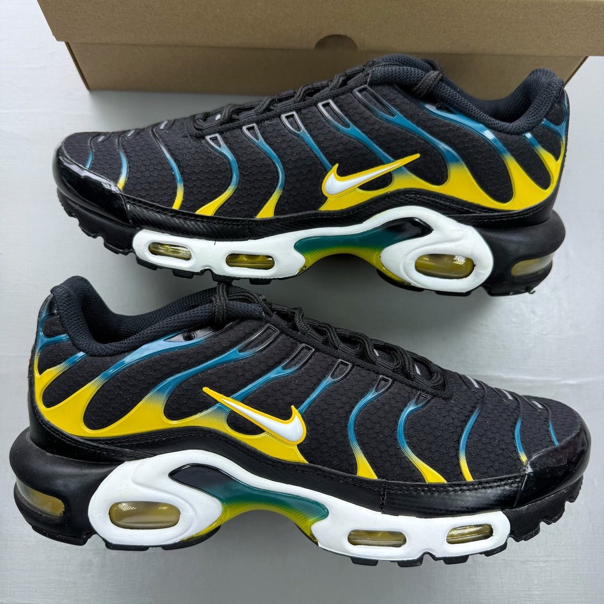 Nike Air Max Plus TN black trainers with teal and yellow accents, featuring logo detailing.