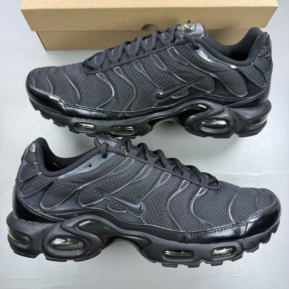 Nike Air Max Plus TN black trainers with distinctive wave pattern and logo detail.