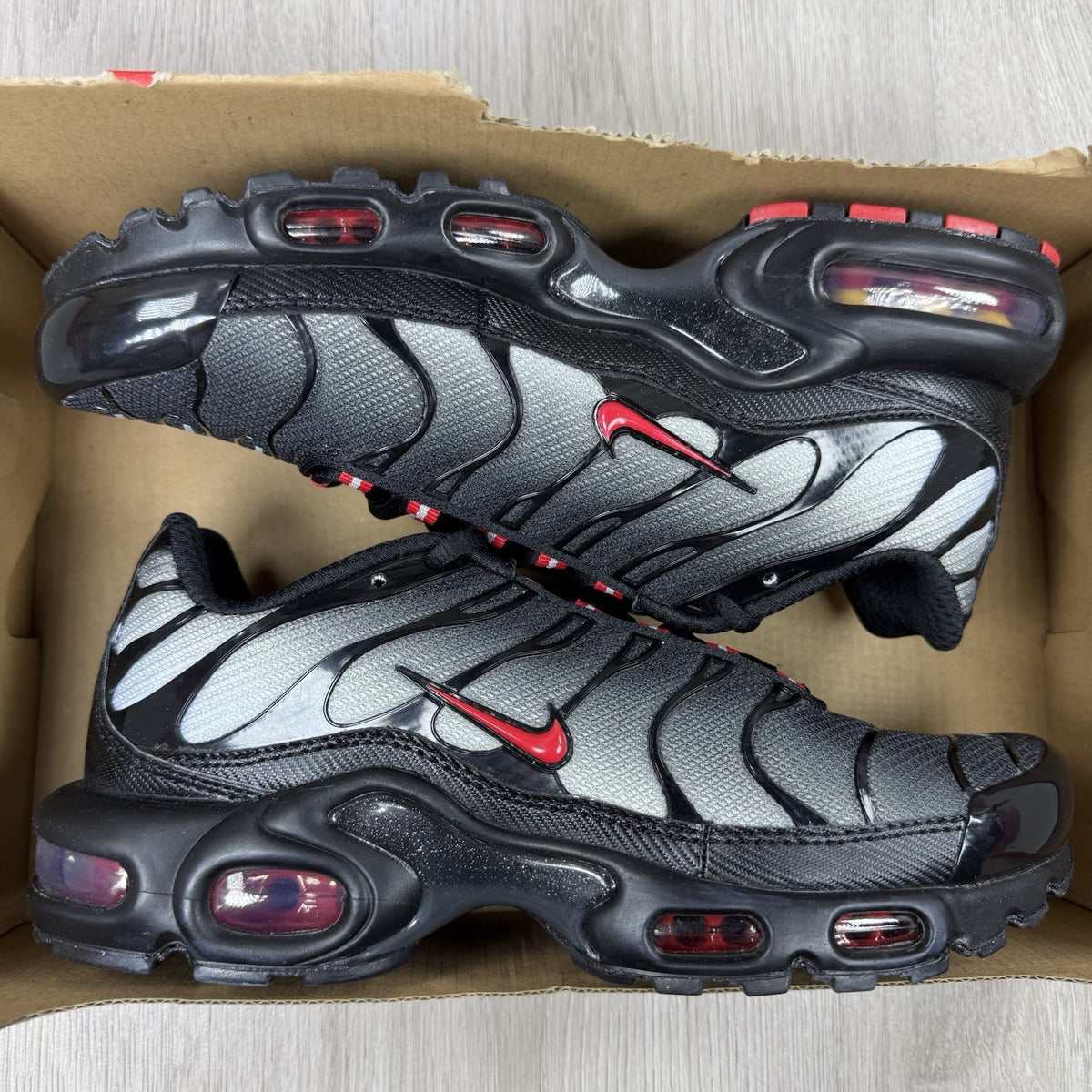 Nike TN Air Max Plus trainers black with red gradient and signature logo design.