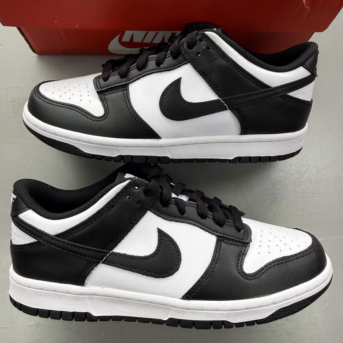 Nike Dunk Low white and black sneakers with retro panda design and logo.