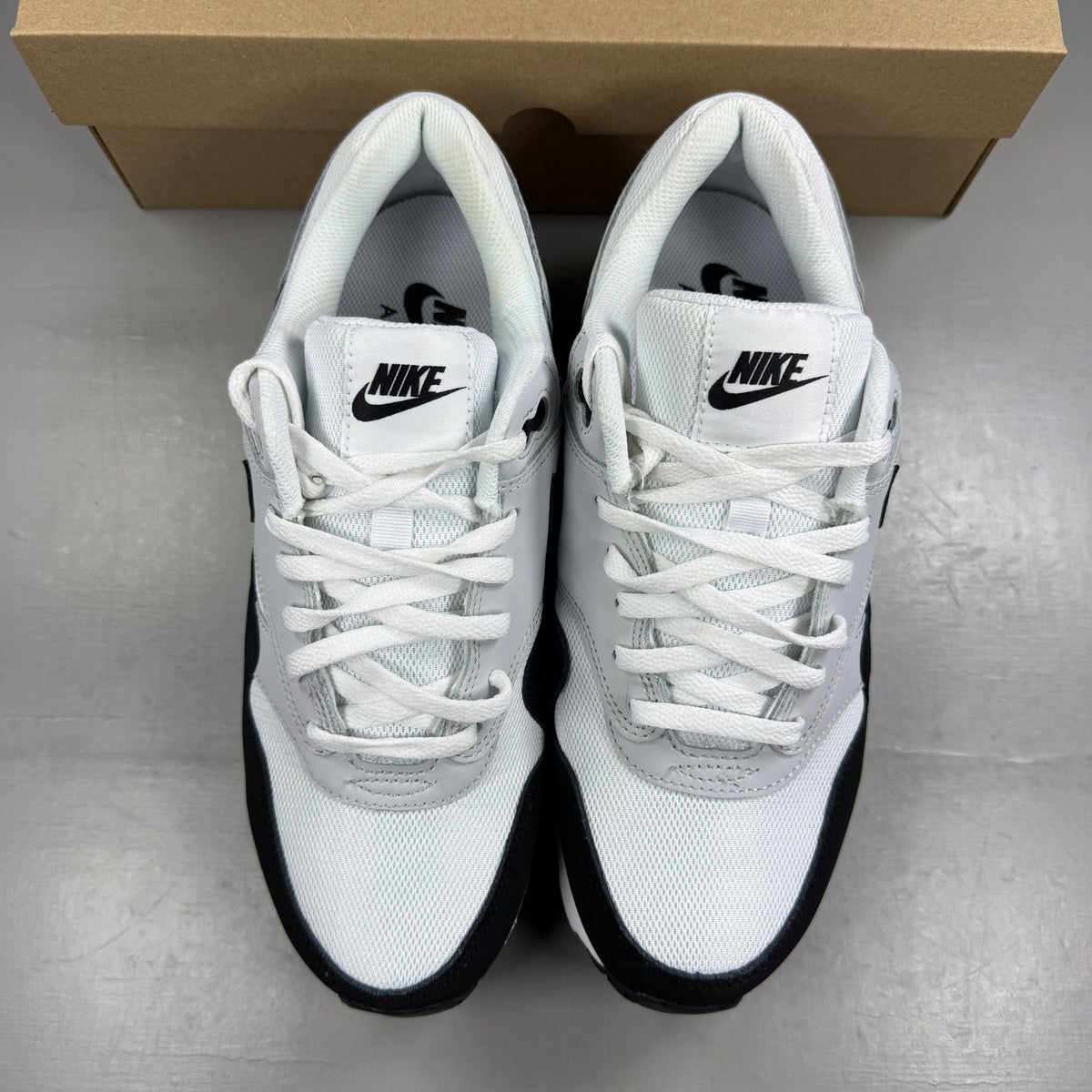 Nike Air Max 1 white trainers with black and grey accents, featuring logo details.