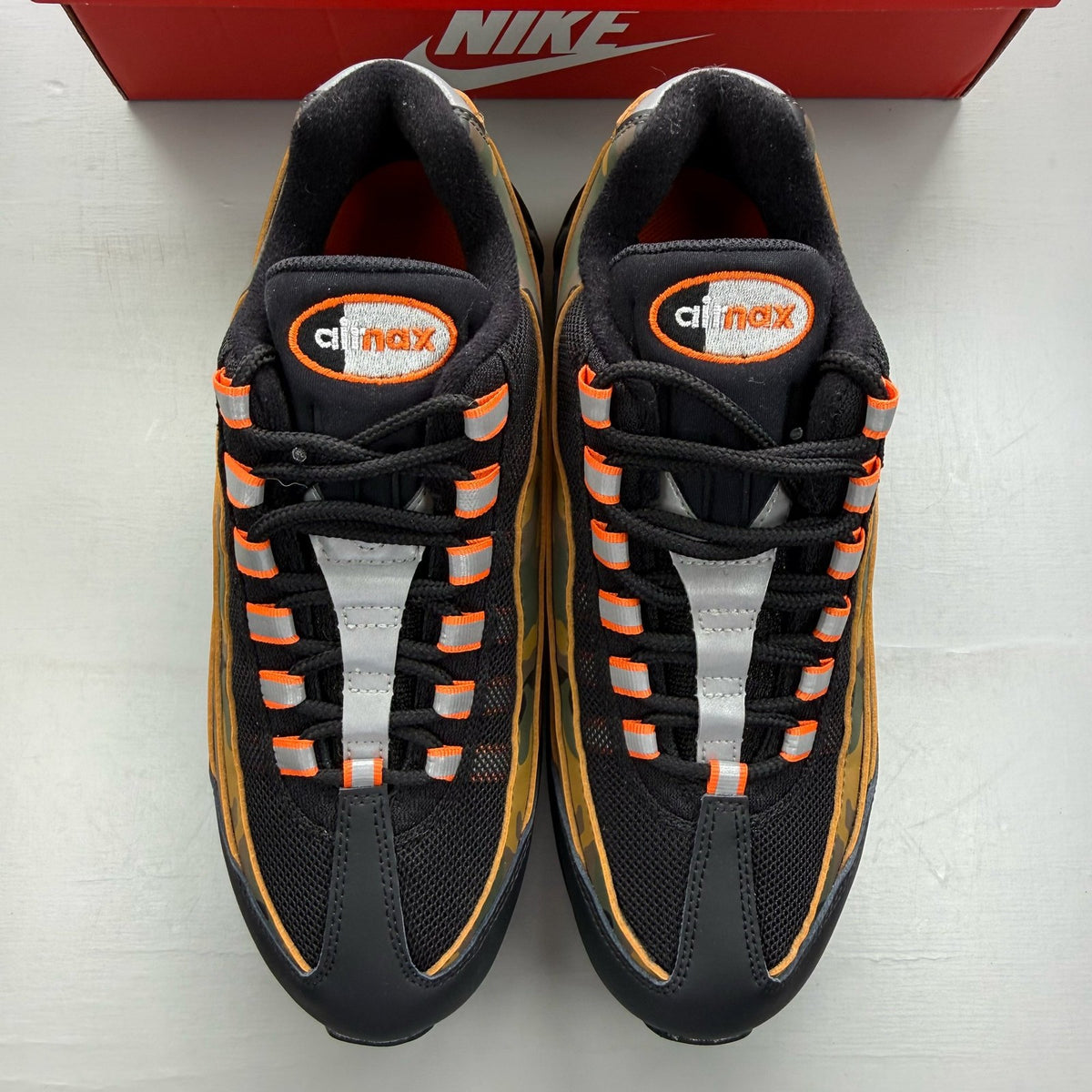 Nike Air Max 95 black trainers with orange camo accents and logo details.