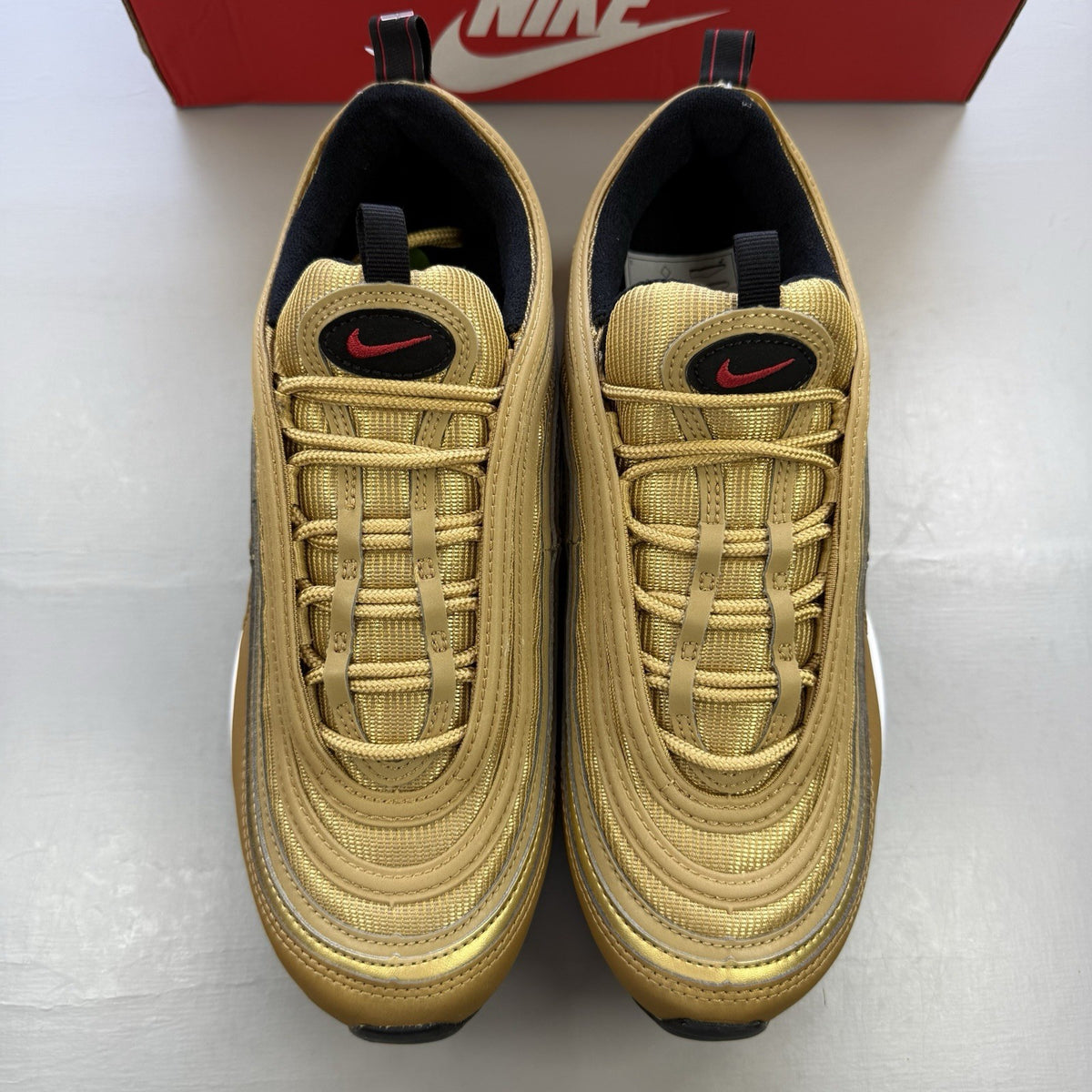 Nike Air Max 97 gold trainers with white and black accents, featuring a sleek design.