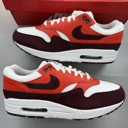 Nike Air Max 1 white trainers with burgundy and red accents, featuring logo details.