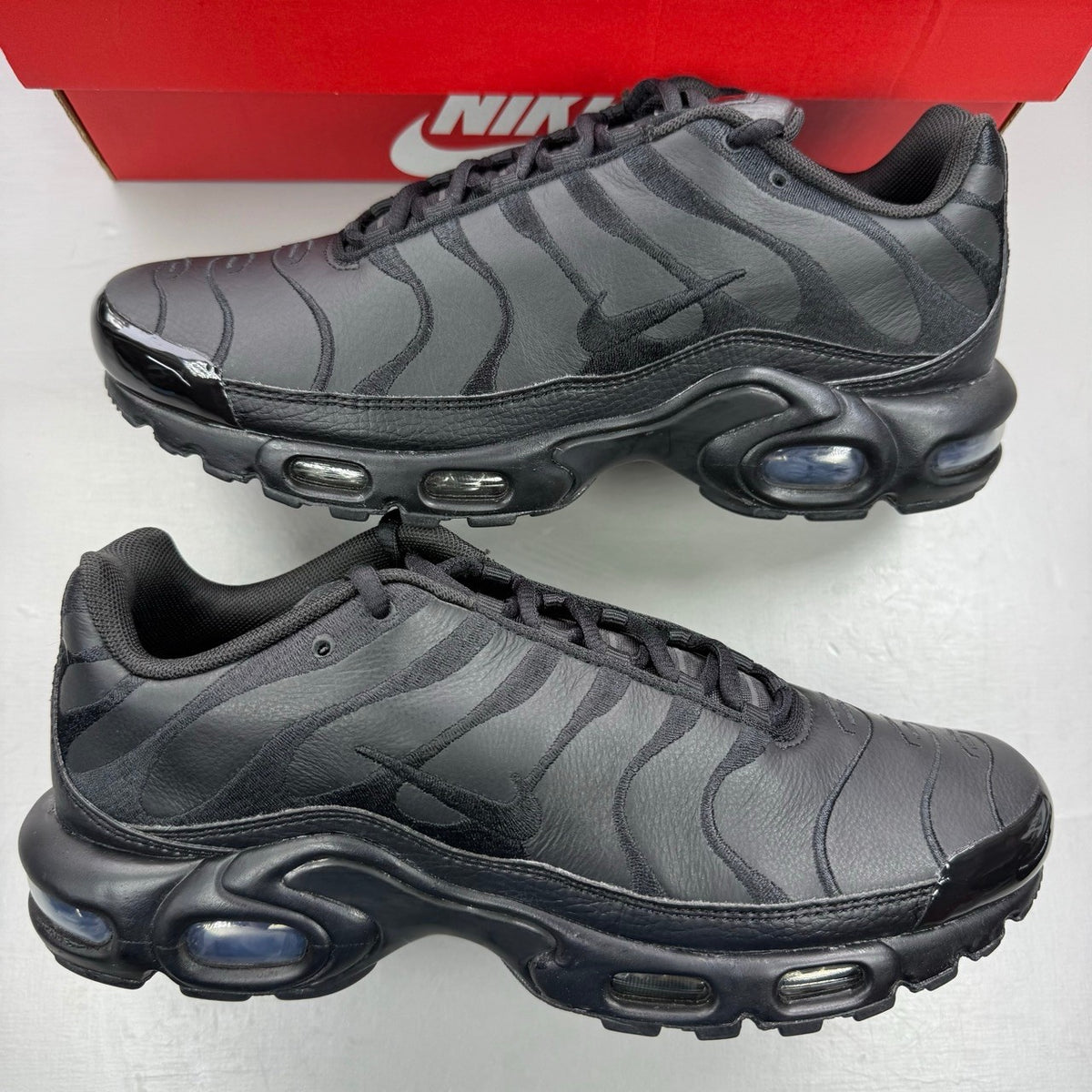 Nike Air Max Plus TN black leather trainers with distinctive wave pattern and logo.