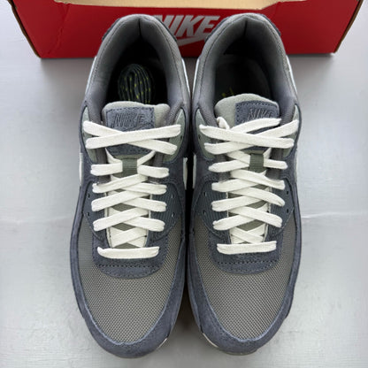 Nike Air Max 90 PRM grey trainers with white accents and distinctive logo details.