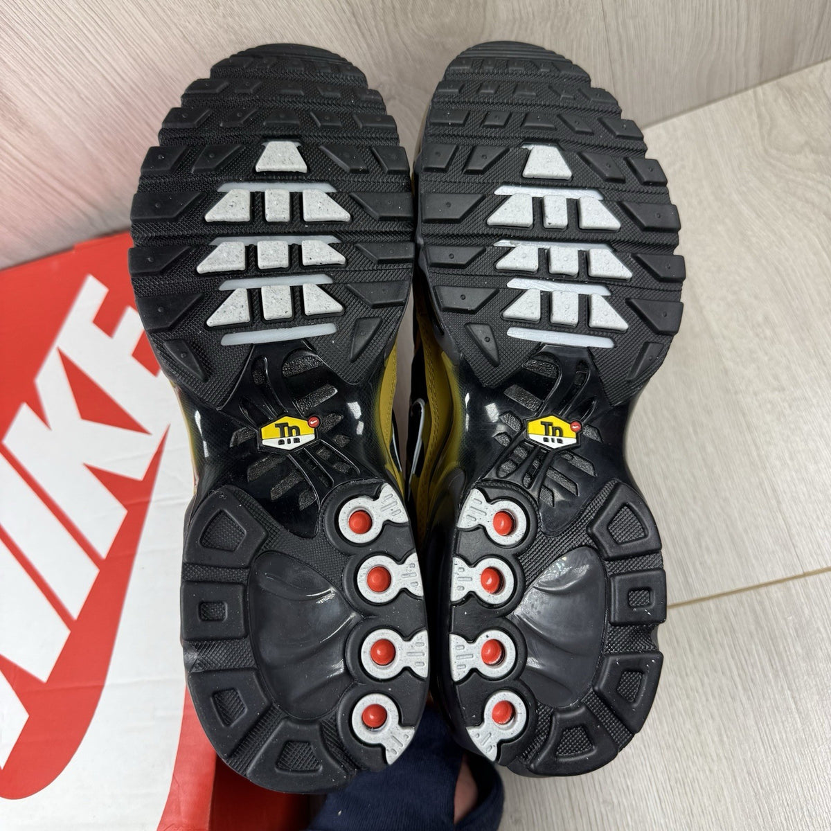 Nike Air Max Plus TN trainers black with gold accents and distinctive wavy pattern.