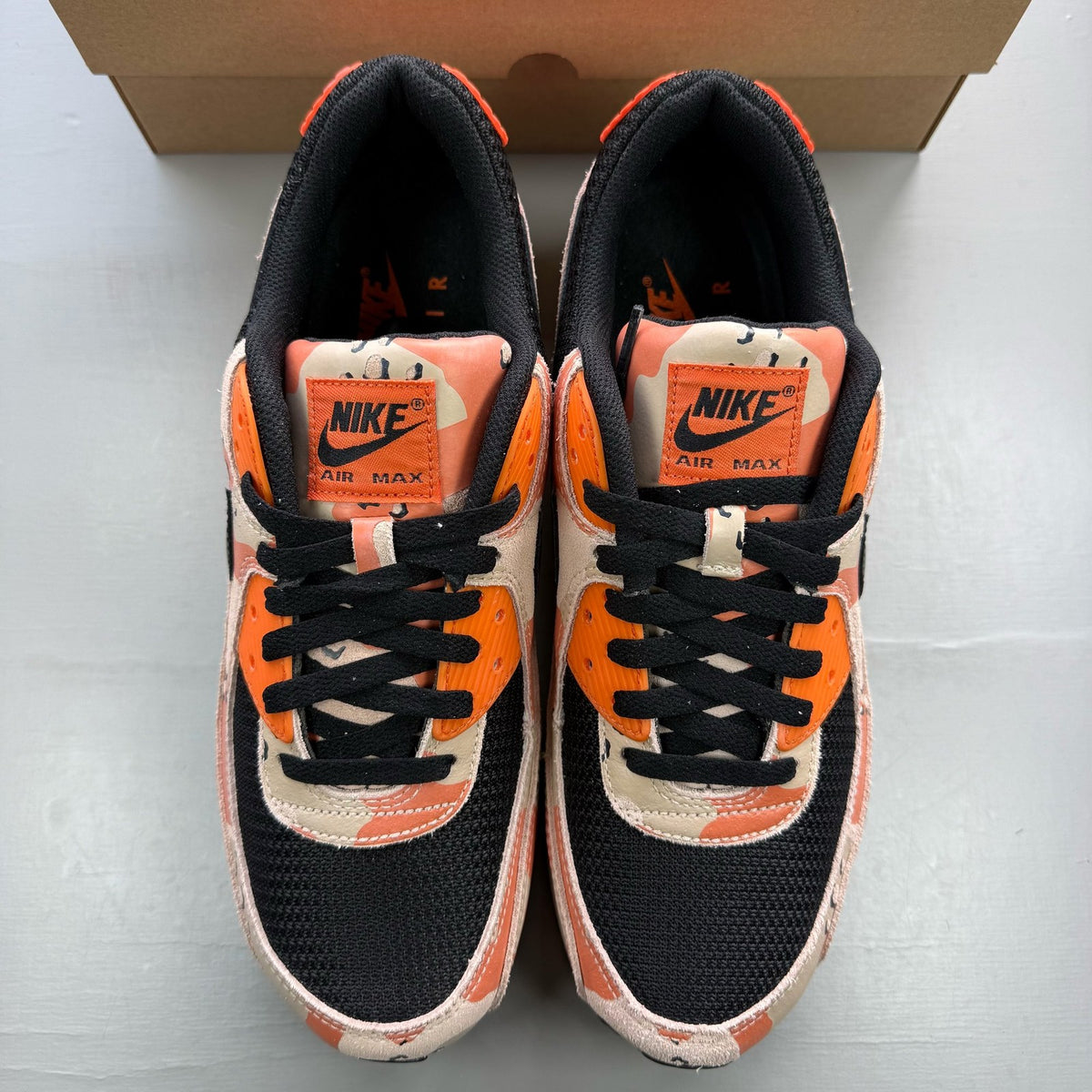 Nike black trainers with camo pattern and orange accents, featuring premium materials.