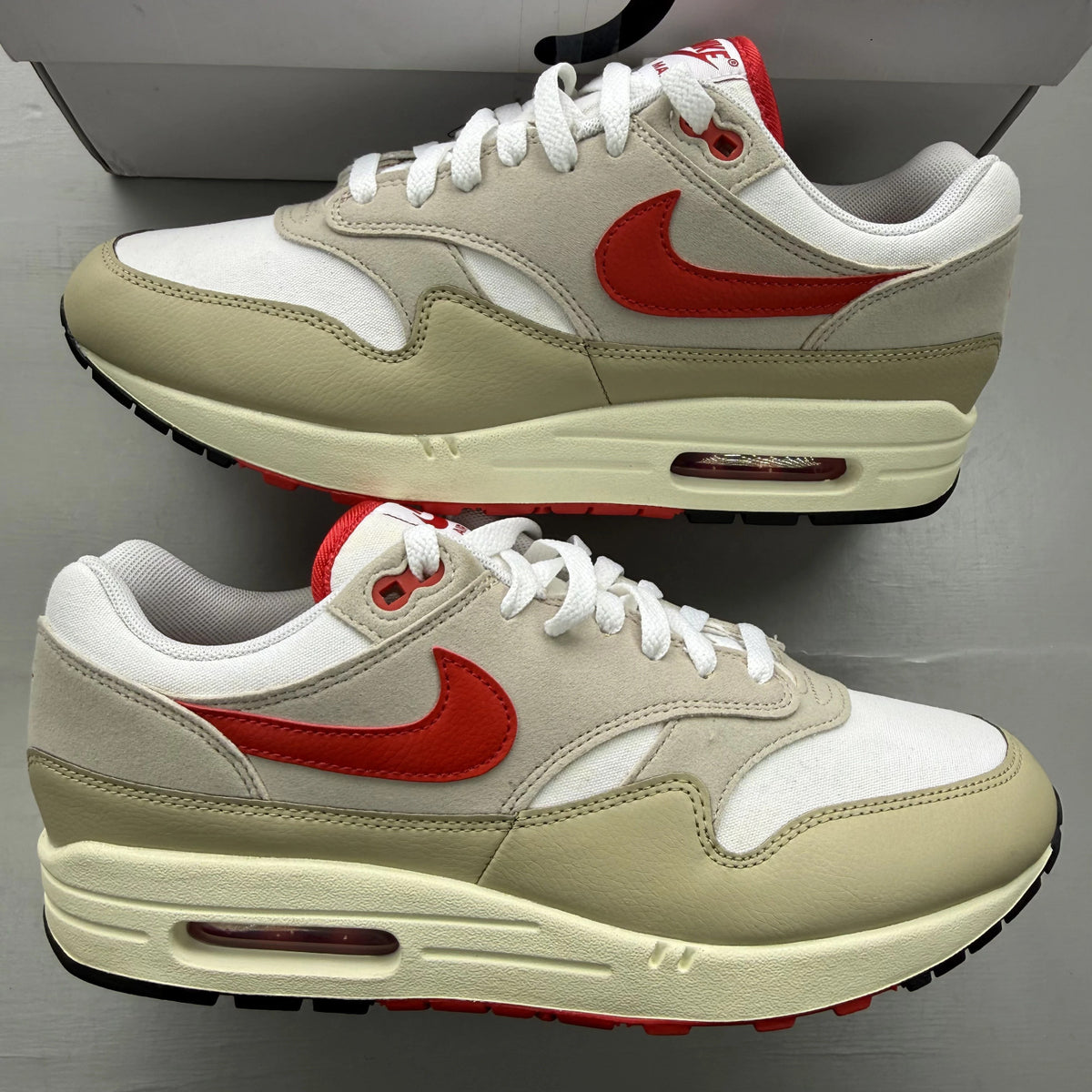Nike Air Max 1 white trainers with red accents and classic logo detailing.