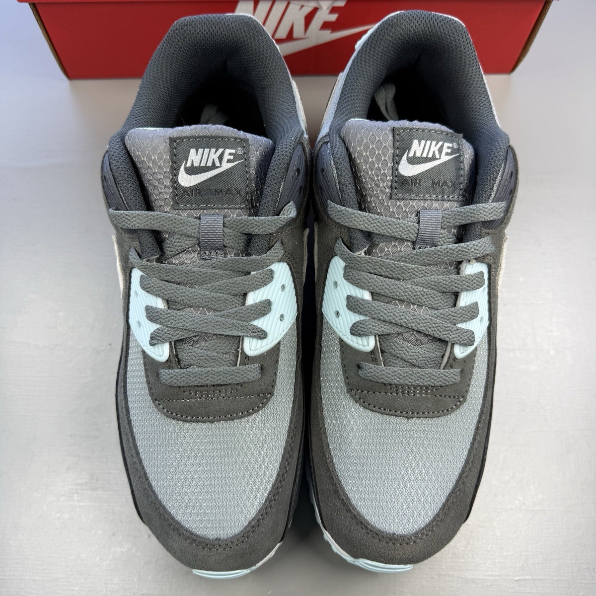 Nike Air Max 90 grey trainers with blue and white accents, featuring iconic logo.