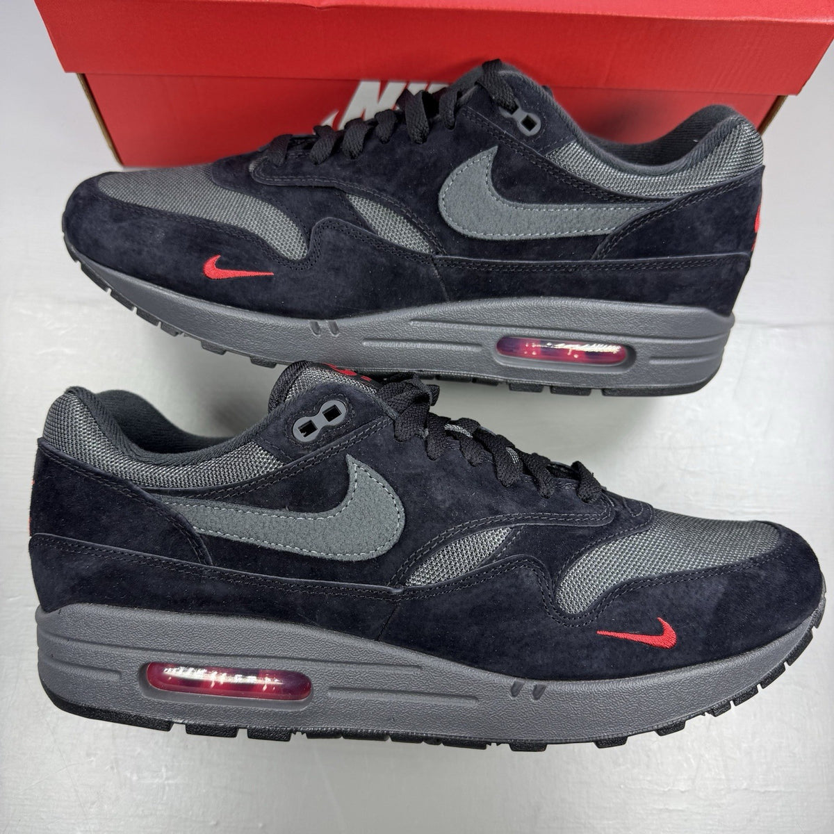 Nike Air Max 1 trainers black with red accents and logo detail on the side.