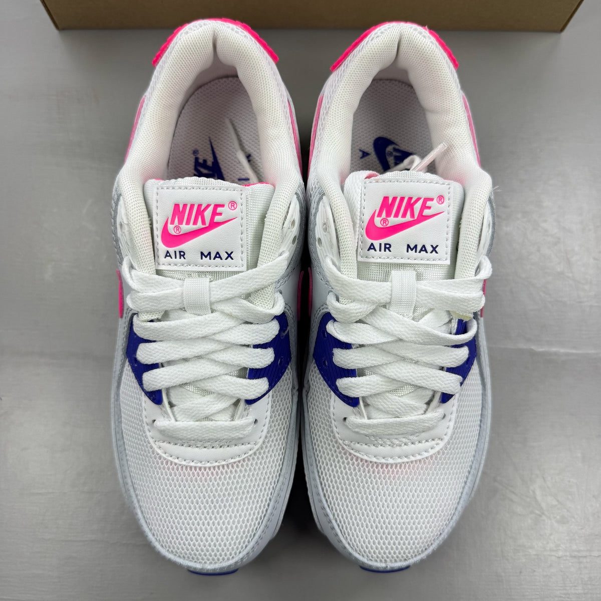 Nike Air Max 90 white trainers with purple and pink accents, featuring logo details.