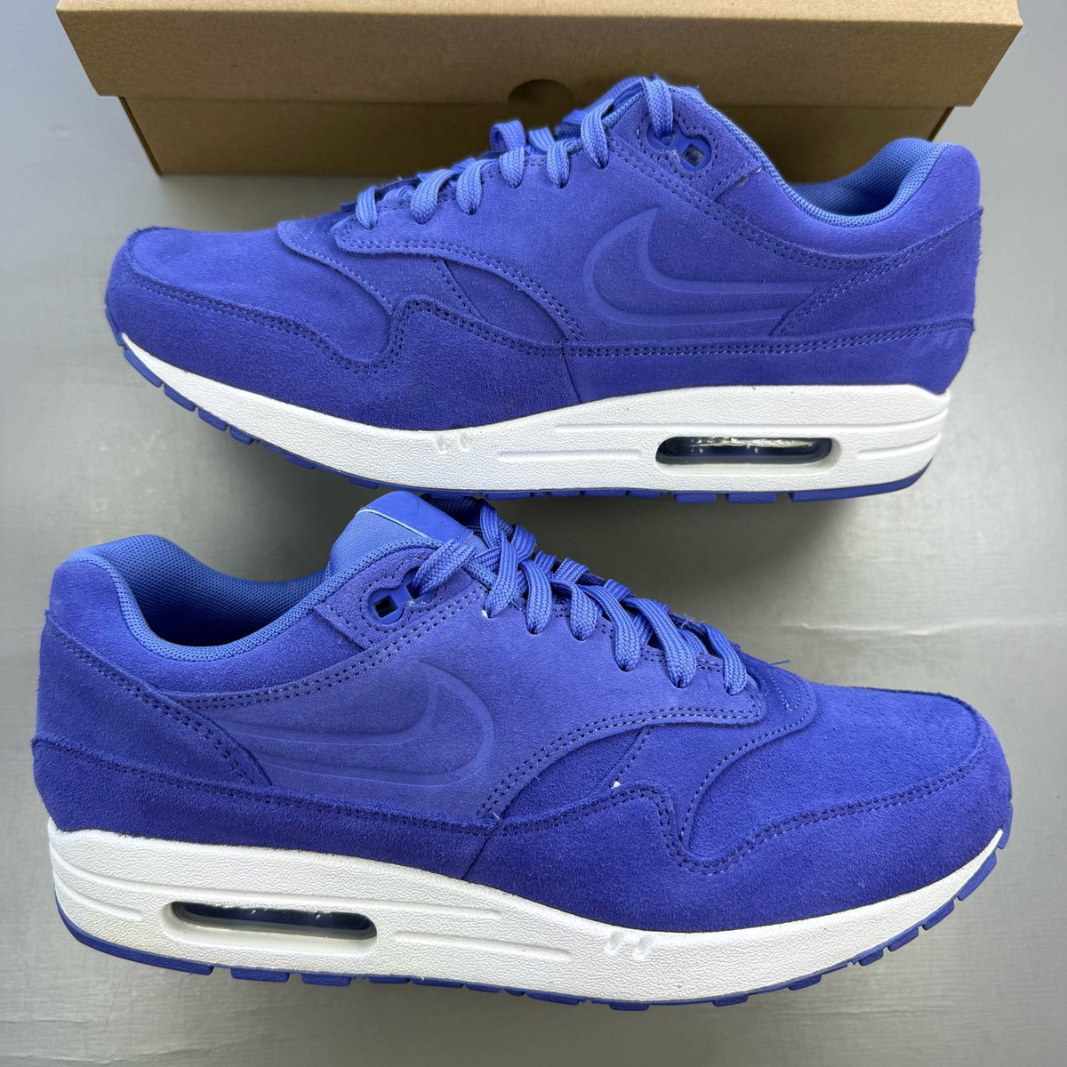 Nike Air Max 1 blue suede trainers with white accents and logo detail.