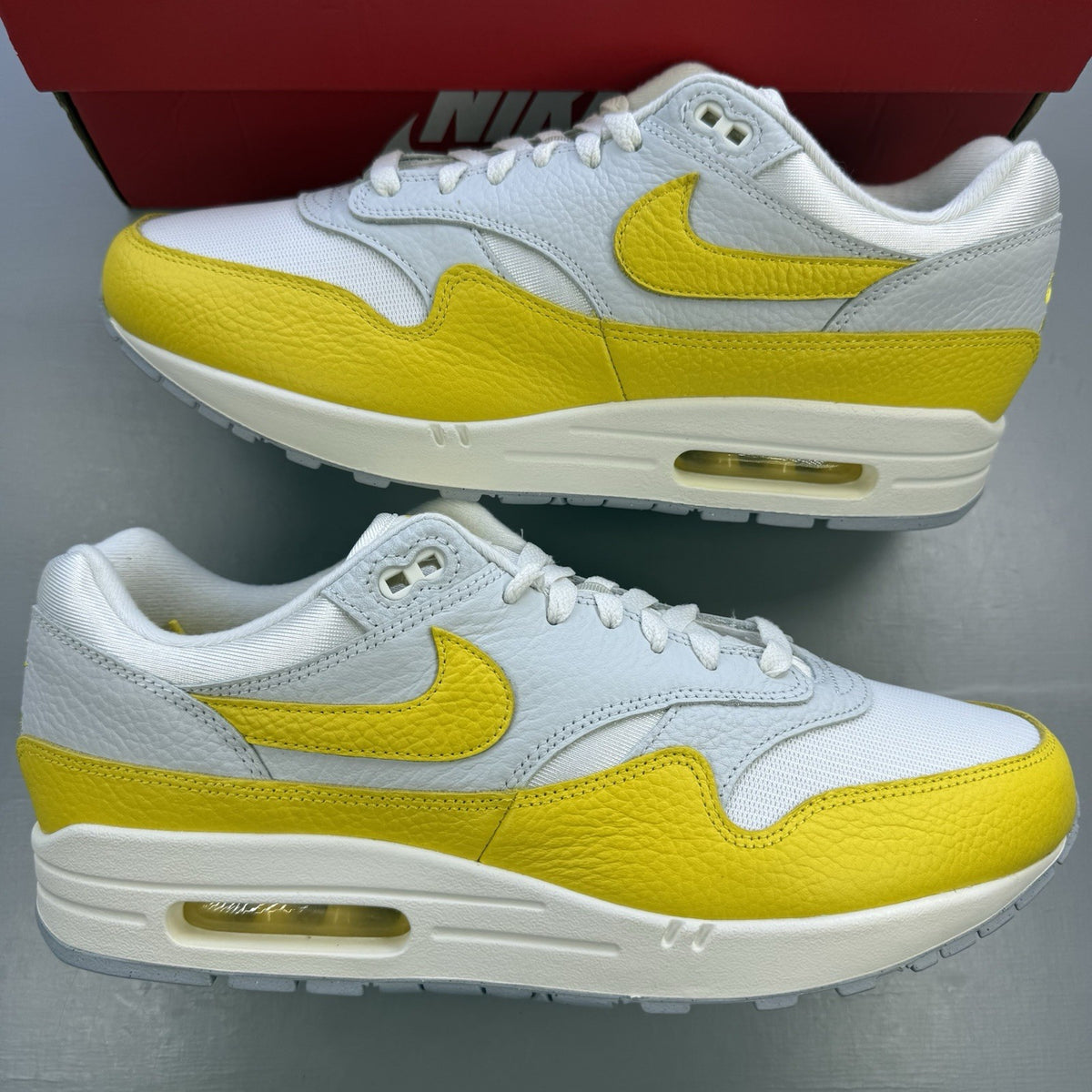 Nike Air Max 1 white trainers with yellow accents and grey detailing.