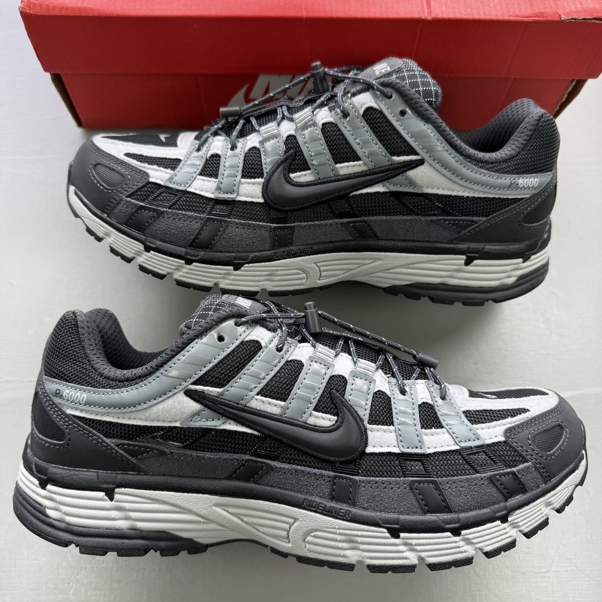 Nike black trainers with grey accents and reflective detailing, featuring a classic logo.