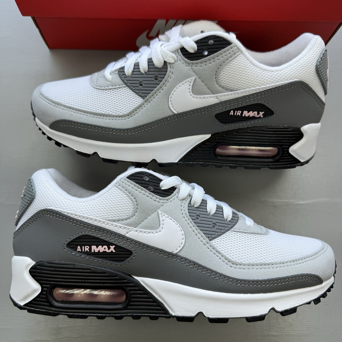 Nike Air Max 90 white trainers with pink foam accents and grey detailing.