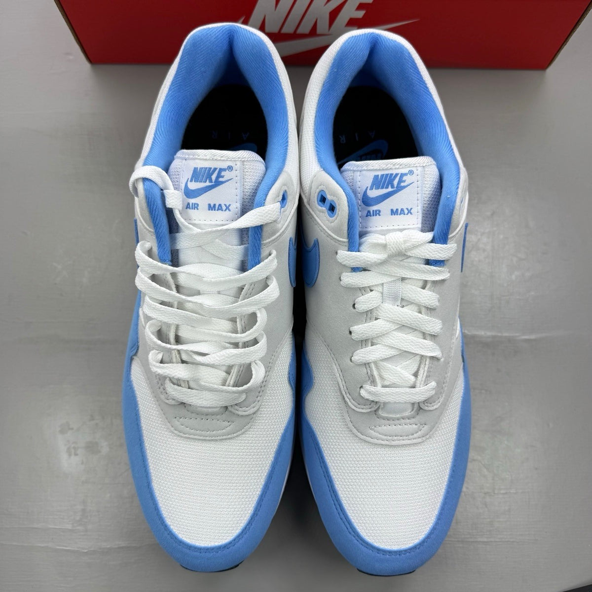 Nike Air Max 1 blue trainers with white accents and UNC logo detailing.